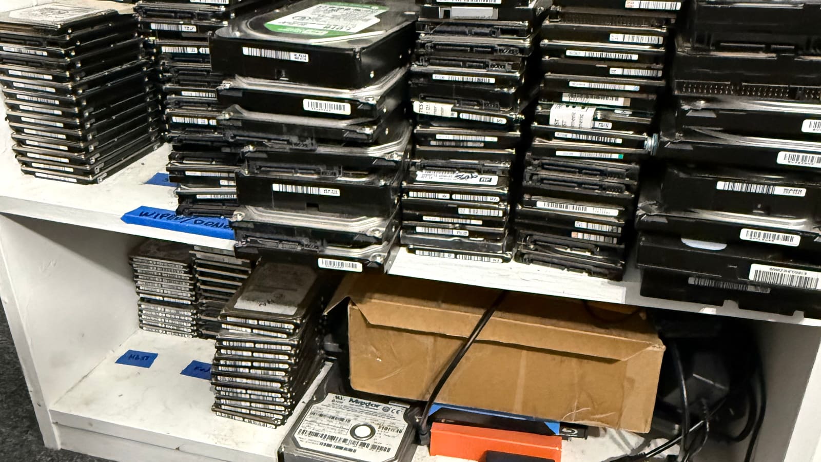 Donor hard drive inventory at The Attic Lab: labeled shelves of 3.5-inch and 2.5-inch drives used for PCB and parts matching