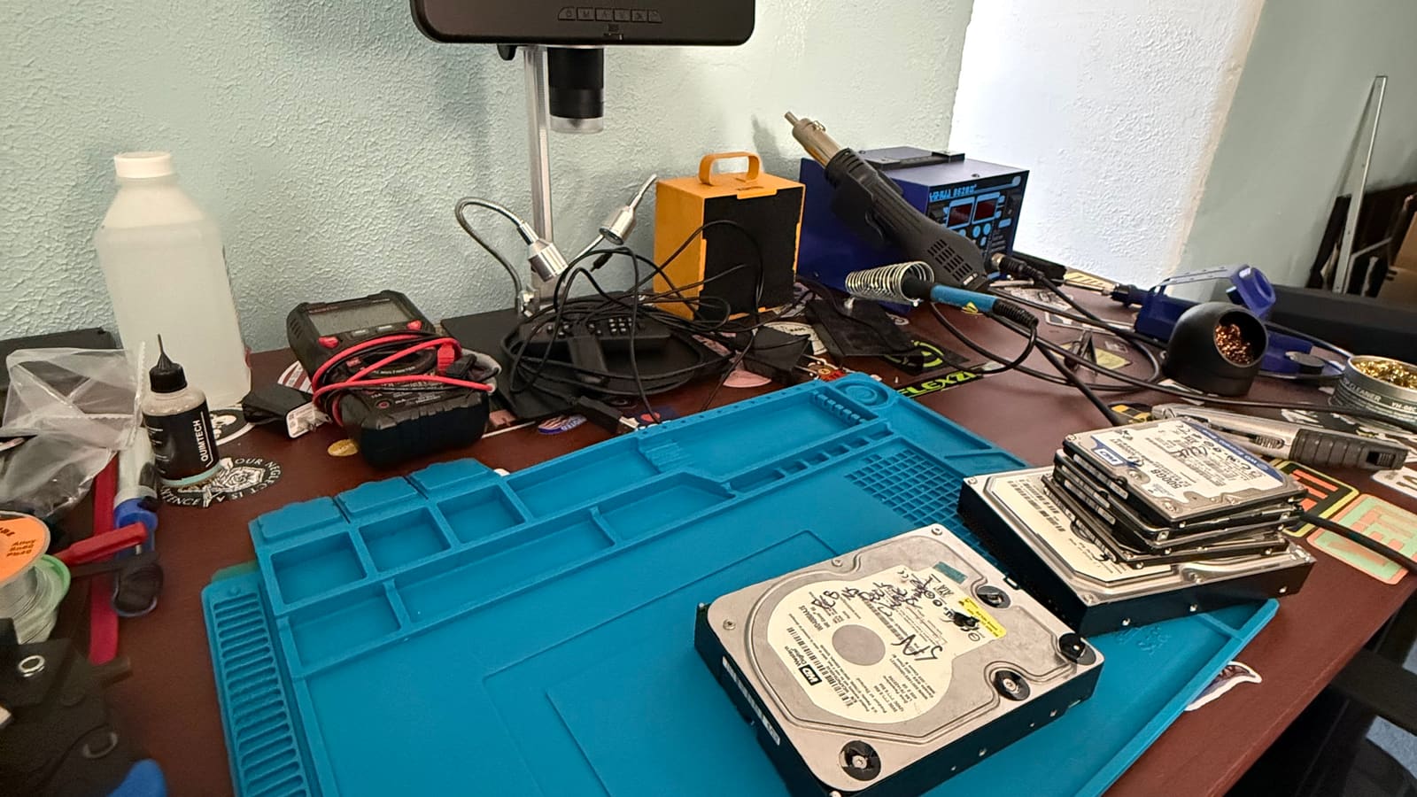 Board-level rework bench at The Attic Lab: digital microscope, hot air station, multimeter, and hard drives staged on an anti-static mat